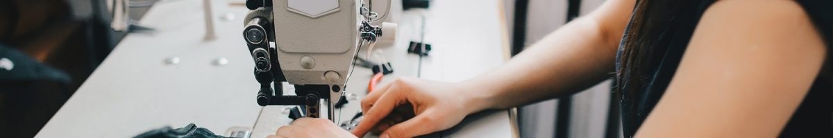 Female artisan threading black leather on sewing machine, close up